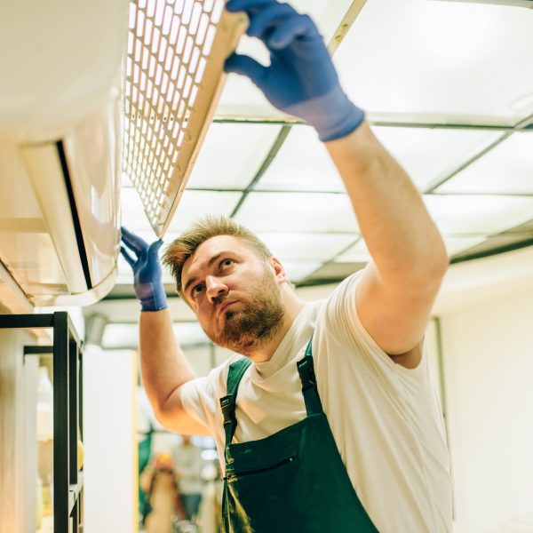 Repairman in uniform repairs the air conditioner Repairman in uniform repairs the air conditioner