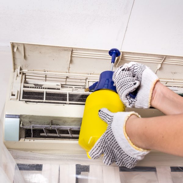 Technician spraying chemical water onto air conditioner grid to Technician spraying chemical water onto air conditioner grid to
